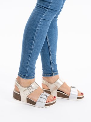 Feet wearing silver platform sandals with buckles, paired with blue skinny jeans, standing on a white background.