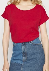 T-shirt rosso a maniche corte con scollatura tonda, abbinato a una gonna di jeans a vita alta. Il tessuto sembra morbido con una consistenza liscia.