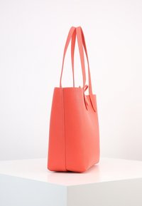 Korale torba na ramię wykonana z teksturowanej skóry, z dwoma wydłużonymi uchwytami i usztywnionym prostokątnym kształtem. Zamek błyskawiczny niewidoczny.