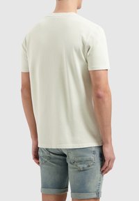 Hellgrünes T-Shirt mit kurzen Ärmeln und Rundhalsausschnitt, glatter Textur und lässigem Schnitt, kombiniert mit hellblauen Jeansshorts.