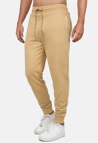 Beige joggings met een elastische tailleband, verstelbaar trekkoord en geribde boorden. Voorzien van subtiele geborduurde logo's aan de zijkant.