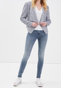 Blazer texturé bleu marine et blanc avec une coupe ajustée, associé à un jean slim bleu clair et des baskets blanches, présenté sur un fond blanc.
