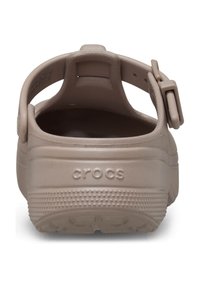 Zoccoli Crocs beige con finitura texturizzata, cinturino posteriore con fibbia regolabile e logo impressa sul tallone. Superficie interna liscia.