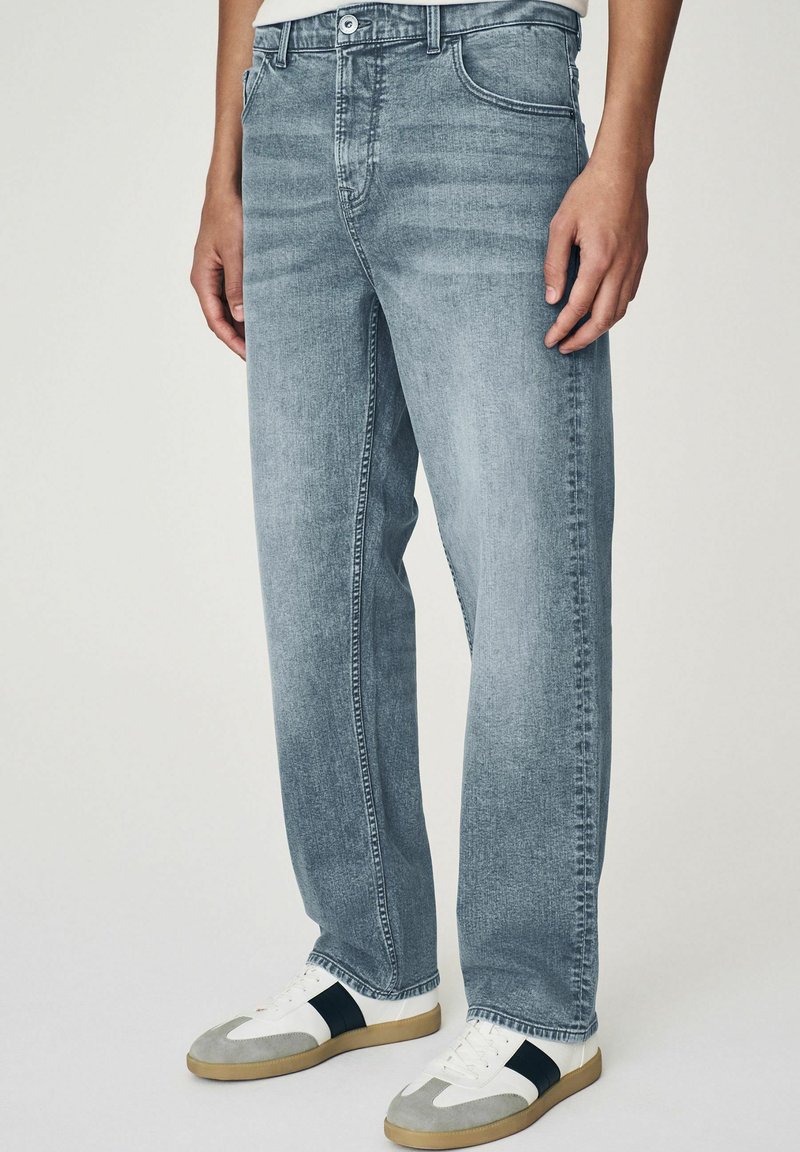 Jeans in denim grigio chiaro con una vestibilità comoda, dotati di cinque tasche, passanti per cintura e leggeri effetti sbiaditi, abbinati a sneakers bianche e grigie.