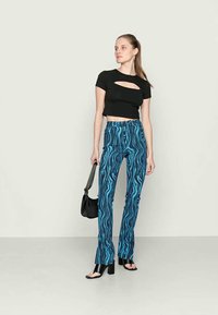 Top preto cropped com detalhe recortado, combinado com calças azuis de cintura alta com um padrão ondulado e acessórios pretos.