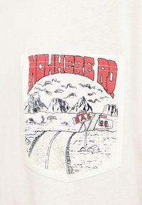 Route désertique avec montagnes en arrière-plan, station-service avec panneau « 1 mile », et grand texte rouge « NOWHERE RD » au-dessus de la scène.