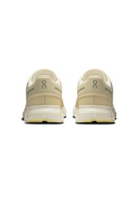 Beige jooksujalatsid, millel on pehme kangas, pehmendustega kaelus ja paks, tekstuuriga tallaosa hallide aktsentidega ning logo detailiga kandadel.
