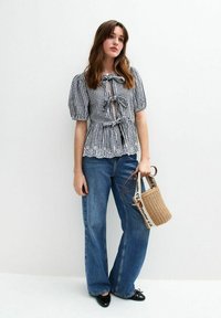 Top de cuadros vichy en blanco y negro con mangas cortas, lazo en la cintura y dobladillo con volantes, combinado con unos jeans de mezclilla azul de tiro alto y pernera acampanada, y un bolso de mimbre.