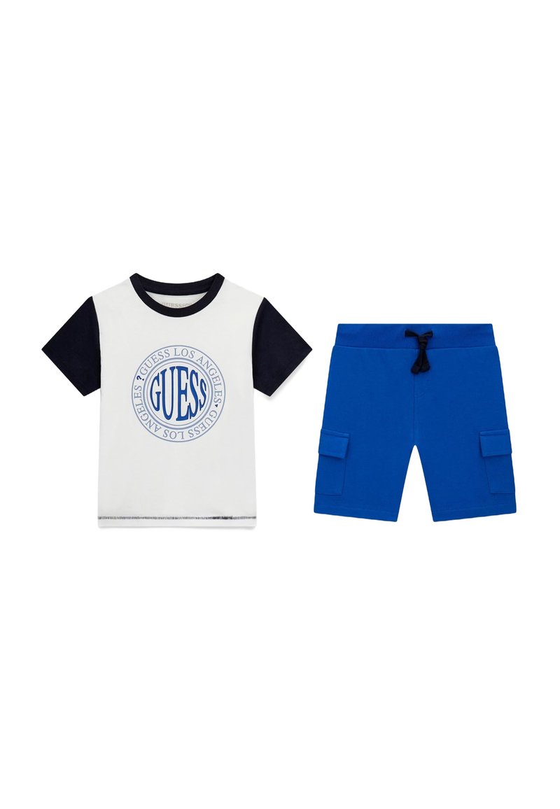 T-shirt bianco con maniche blu navy e logo rotondo, abbinato a pantaloni cargo blu, dotati di tasche laterali e cintura elastica.