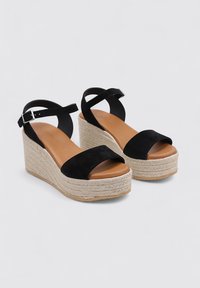 Sandalias de cuña de ante negro con una tira sobre los dedos y una tira en el tobillo, que cuentan con una plataforma de esparto texturizada y una plantilla de cuero suave.