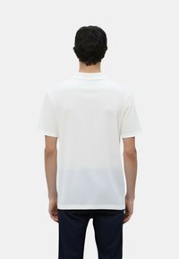 Polo shirt bianco con maniche corte e colletto a punta; realizzato in tessuto liscio con una leggera lucentezza e vestibilità rilassata.