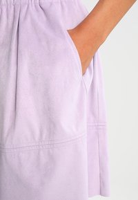 Lila sammetsskjol med sidofickor, rynkad midja och subtila sömdetaljer längs fållen för extra textur.