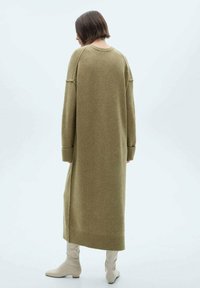 Abito lungo di maglia verde oliva con una vestibilità comoda, polsini e orlo a costine. Il materiale sembra morbido e testurizzato, arrivando sotto le ginocchia.