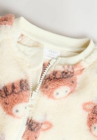 Helle Babyjacke in Cremefarbe, aus weichem Plüschmaterial, mit pinkem Tierdruck, Reißverschluss vorne und geripptem Kragen. Markenetikett sichtbar.