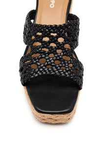 Sandale wedge en cuir tressé noir avec un orteil ouvert, plateforme en jute et semelle intérieure en cuir noir lisse. Design tissé complexe sur les brides.