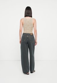 Beige strikket topp med mønster, kombinert med høyt midje, vide mørkegrå jeans. Merker med detaljer på baklommene er synlige.
