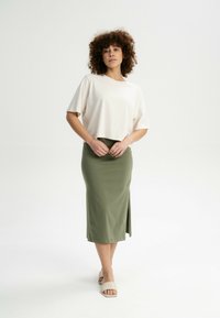 Licht beige cropped t-shirt gecombineerd met een aansluitende olijfgroene midi rok met een zijsplit. Het model draagt beige slipper sandalen.