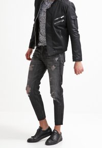 Chaqueta de cuero negra con cremalleras plateadas, camisa con estampado, jeans negros desgastados y zapatillas negras. Corte moderno y materiales texturizados.