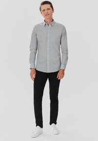 Koszula z długim rękawem w szaro-białą kratę, zestawiona z czarnymi spodniami slim-fit i białymi sneakersami. Gładki bawełniany materiał.