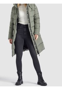 Puffer coat in olive green with a zip closure and drawstring hood, paired with black skinny jeans and lace-up black combat boots.