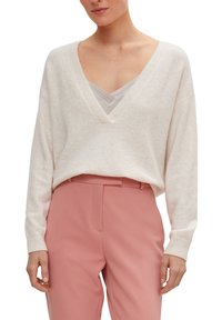 Pull crème à col en V avec manches longues et coupe décontractée, associé à un pantalon ajusté rose pâle. Texture douce et design simple.