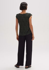 Top nero con maniche a cappuccio, caratterizzato da un motivo a pois colorati. Abbinato a pantaloni larghi neri a gamba larga. Tessuto liscio, design casual.