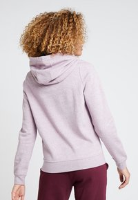 Ljuslila sweatshirt med luva, mjukt tyg, långa ärmar, ribbade muddar och fåll. Bärs med vinröda byxor som visar en avslappnad passform.