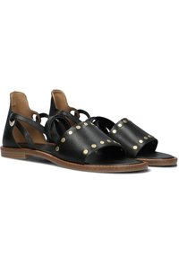 Zwarte leren sandalen met uitsnijdingen, ronde gouden studs en een platte houten zool. Open neus met verstelbare bandjes.