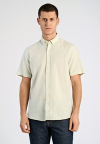 Camicia a maniche corte con bottoni in tessuto verde chiaro. Presenta una texture morbida, colletto a punta e bottoni bianchi, abbinata a jeans scuri.