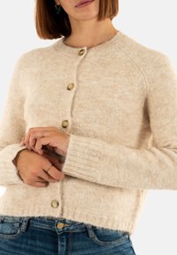 Cardigan in lana beige chiaro con scollo rotondo, polsini a coste e bottoni in legno, caratterizzato da una finitura morbida e testurizzata.