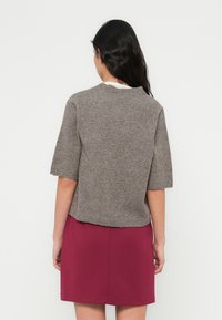 Γκρι πλεκτό πουλόβερ με κοντά μανίκια και στρογγυλή λαιμόκοψη, σε συνδυασμό με φούστα μπορντό. Λεία υφή, άνετη γραμμή και κοντό μήκος.