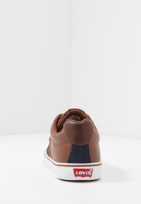 Brązowy skórzany sneaker z akcentami z denimu. Posiada wyściełany kołnierz, białą podeszwę oraz czerwone logo Levi's na pięcie.