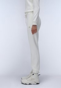 Witte sweatpants met elastische boorden, voorzien van een trekkoord in de taille en zijzakken. Gemaakt in combinatie met witte en grijze hoge sneakers.