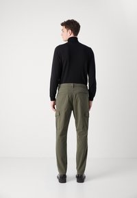Jersey negro de cuello alto para hombres combinado con pantalones cargo verdes oliva que cuentan con múltiples bolsillos; tejido suave con un ajuste ceñido y sutiles acentos de hardware.
