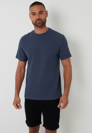 Camiseta de manga corta azul marino con un patrón texturizado, escote redondo y corte relajado, combinada con pantalones cortos negros arremangados.