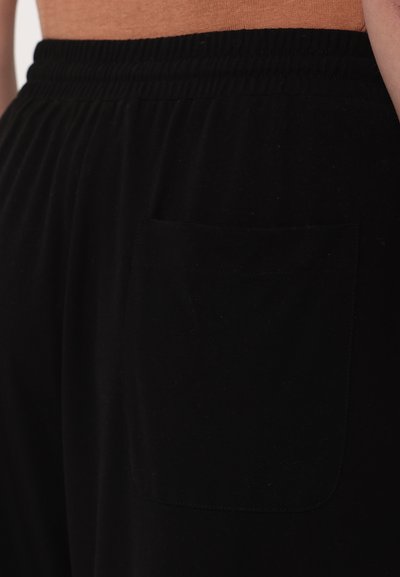 Black pants made of soft fabric, featuring an elastic waistband and a single back pocket. Simple design with no visible patterns.