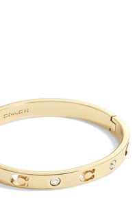 Bracciale in metallo color oro con dettagli a forma di "C" intagliati e quattro cristalli trasparenti incastonati. Presenta una forma elegante e arrotondata e una chiusura a scatto.