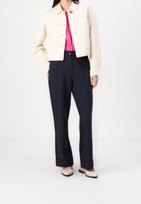 Chaqueta de denim crema recortada sobre una blusa rosa, combinada con pantalones oscuros de corte ala de pato en color azul marino y zapatos beige claros. Texturas suaves y diseño estructurado.