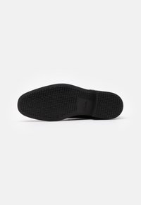 Black rubber shoe sole with a textured surface, featuring a zigzag tread pattern and subtle branding. Flat design, durable and flexible.