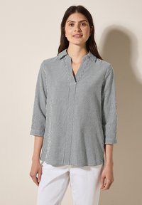 Blusa a righe in navy e bianco, realizzata in tessuto leggero, presenta un colletto a revers, maniche a tre quarti e spiragli laterali all'orlo.