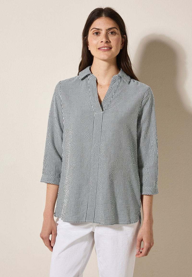 Blusa a righe in navy e bianco, realizzata in tessuto leggero, presenta un colletto a revers, maniche a tre quarti e spiragli laterali all'orlo.