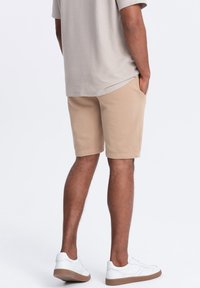 Pantaloni corti beige realizzati in tessuto morbido, dotati di tasche laterali, abbinati a sneakers bianche. La maglietta è grigia chiara con una vestibilità comoda.