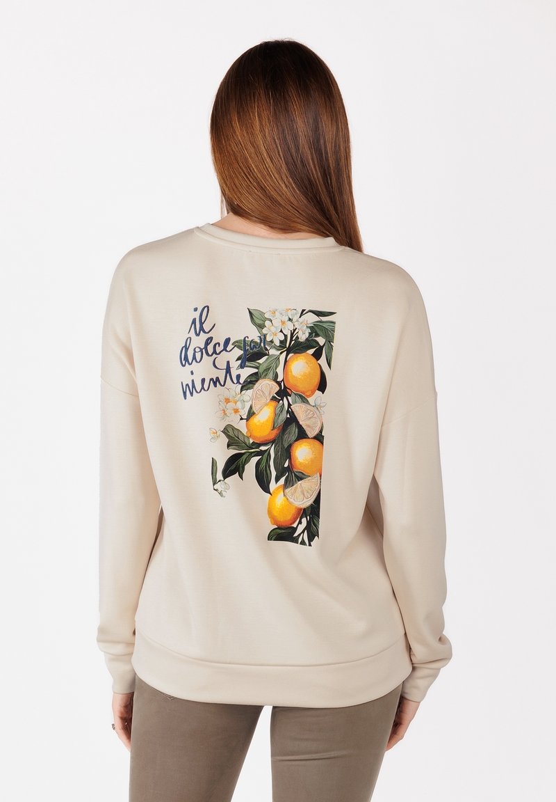 Krämfärgad sweatshirt med en livlig ryggtryck av apelsiner och blommor med texten "il dolce permente." Mjuk tyg, avslappnad passform.