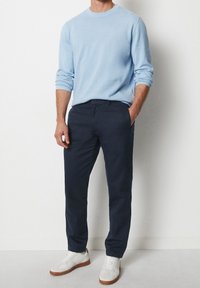 Maglione lavorato a maglia azzurro chiaro, chinos blu scuro e sneakers bianche con accenti marroni. L'outfit presenta una vestibilità comoda e un design semplice.