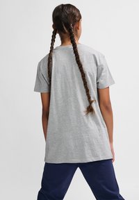 Grå bomulds t-shirt med korte ærmer, afslappet pasform og lige kant. Båret med marineblå bukser; hår stylet i to fletninger.