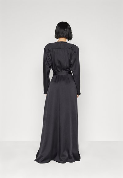 Μαύρο σατέν φόρεμα με στενή μέση, μακριά μανίκια και λεία υφή· διαθέτει πλισέ λεπτομέρεια στην πλάτη και ρέουσα φούστα.
