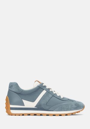 Blå ruskind- og lædersneaker med hvide snørebånd, hvid side detalje og brun gummi sål placeret mod en ensfarvet lys baggrund.