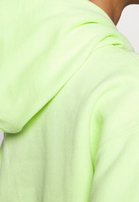Felpa verde chiaro realizzata in un tessuto morbido e testurizzato. Presenta un cappuccio prominente, una cucitura della spalla curva e dettagli a coste sui polsini.