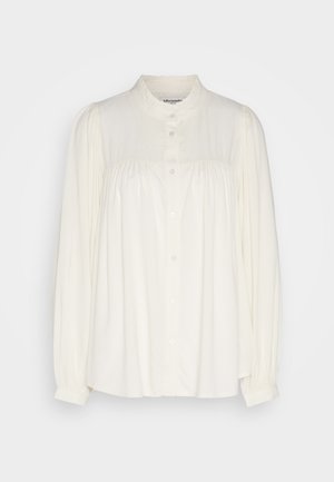 Bílá halenka s dlouhým rukávem, vysokým výstřihem, knoflíkovým zapínáním a nařasenými detaily na ramenou. Vyrobena z lehkého materiálu.