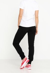 Czarne spodnie dresowe o zwężanym kroju, zestawione z białym t-shirtem i różowymi sportowymi butami z białymi akcentami.